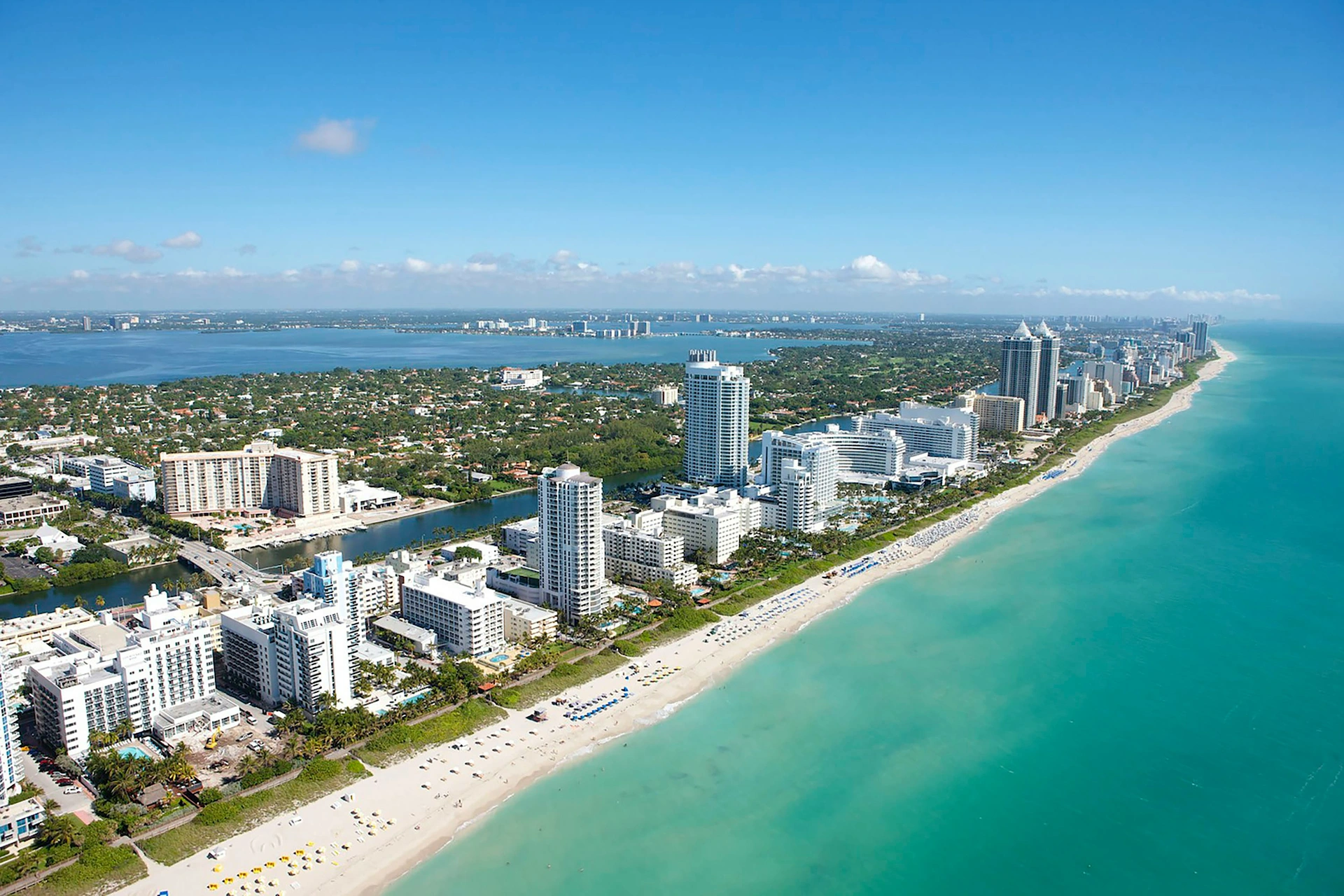 Aerial view of Miami Beach with tall buildings along the coastline and turquoise waters