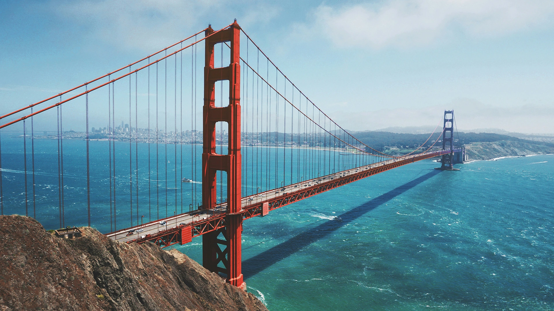 The Golden Gate Bridge with the San Francisco skyline in the background and clear blue water beneath