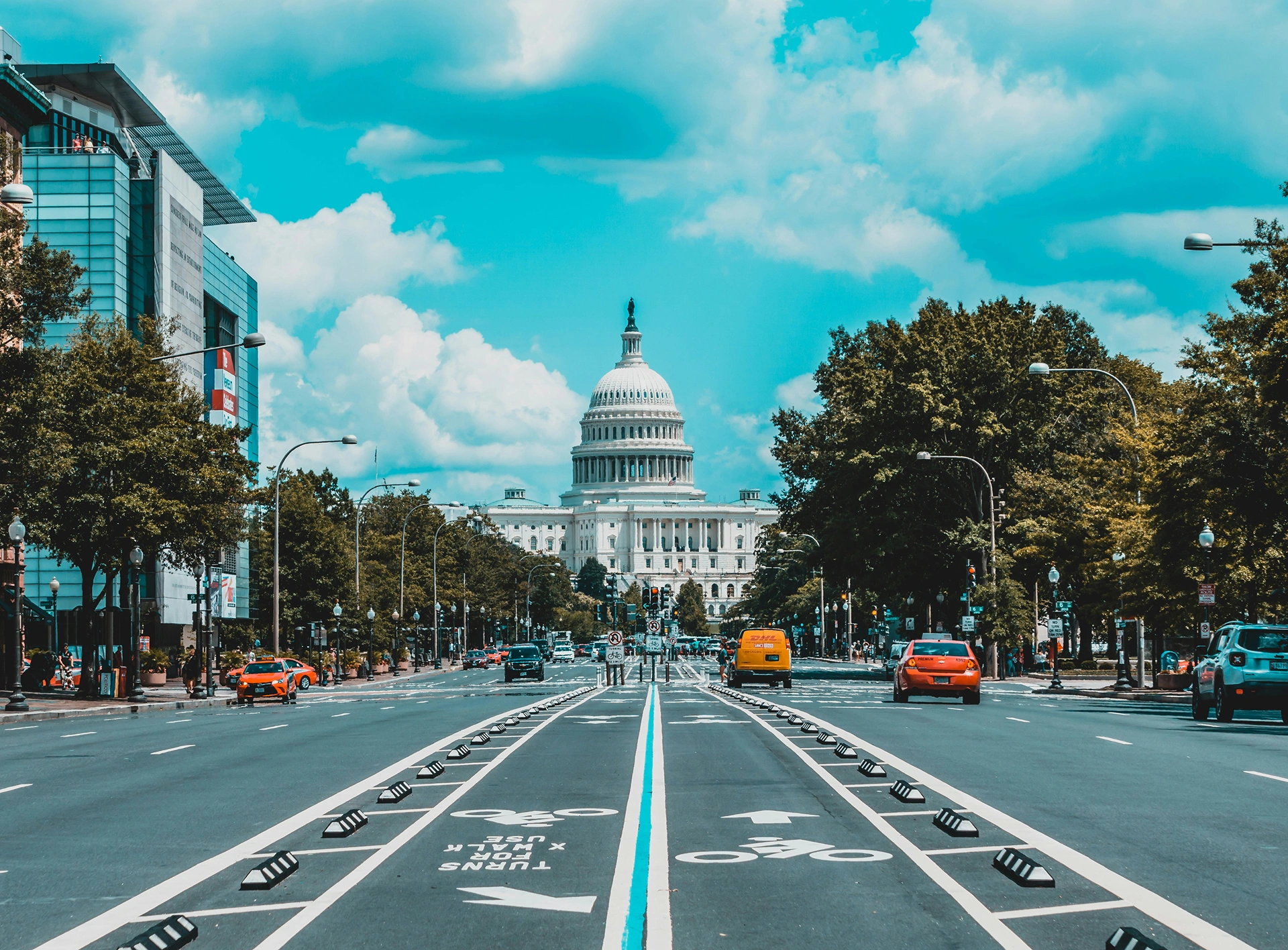 The US Capitol Building stands at the end of a wide avenue with traffic and trees